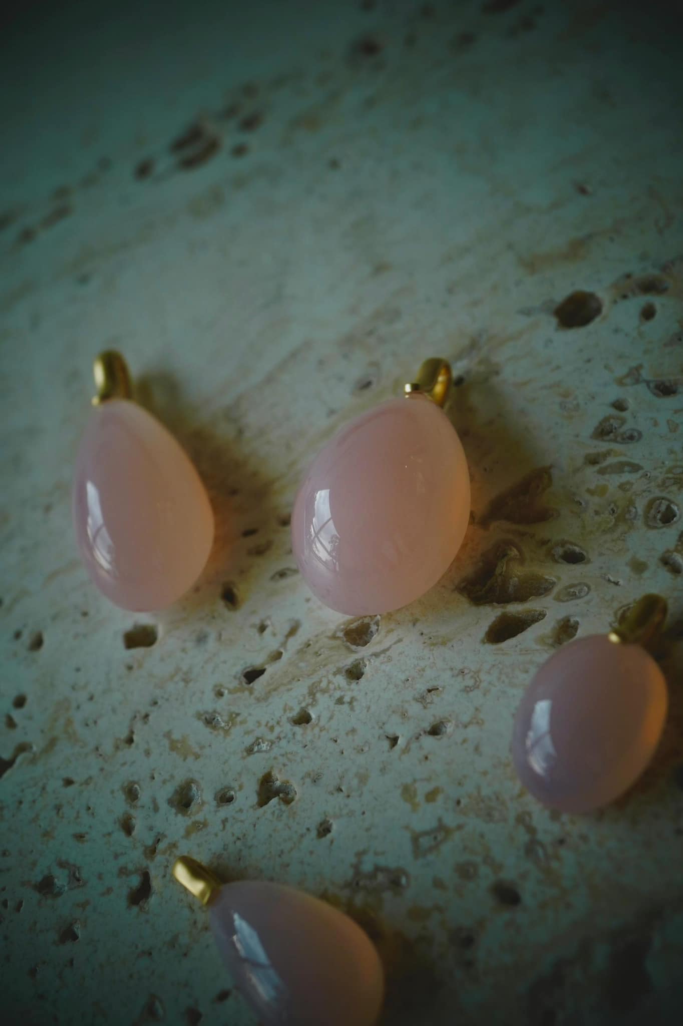Collection of Alaskan rose quartz pendants featuring elegant designs and smooth, polished surfaces on a textured background.