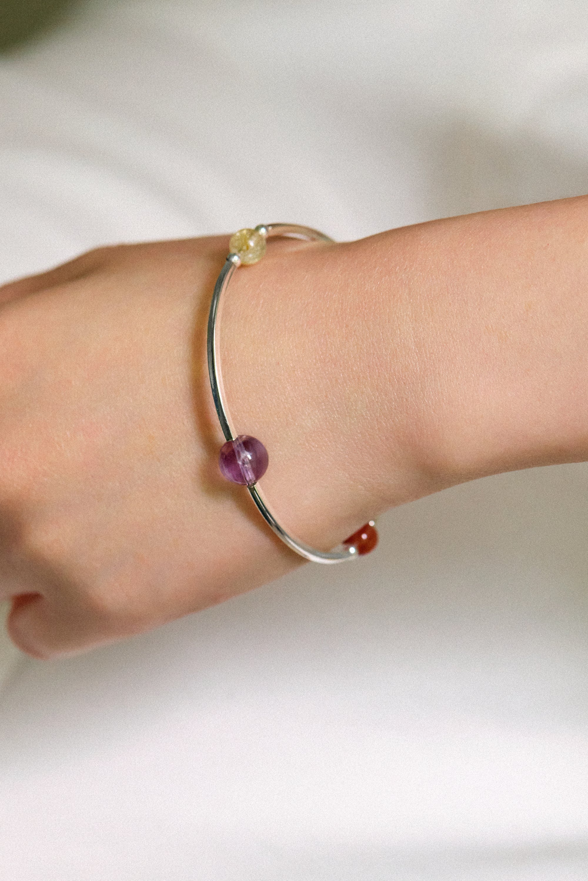 Close-up of a hand wearing the 4Play Bangle featuring colorful gemstones and silver design.