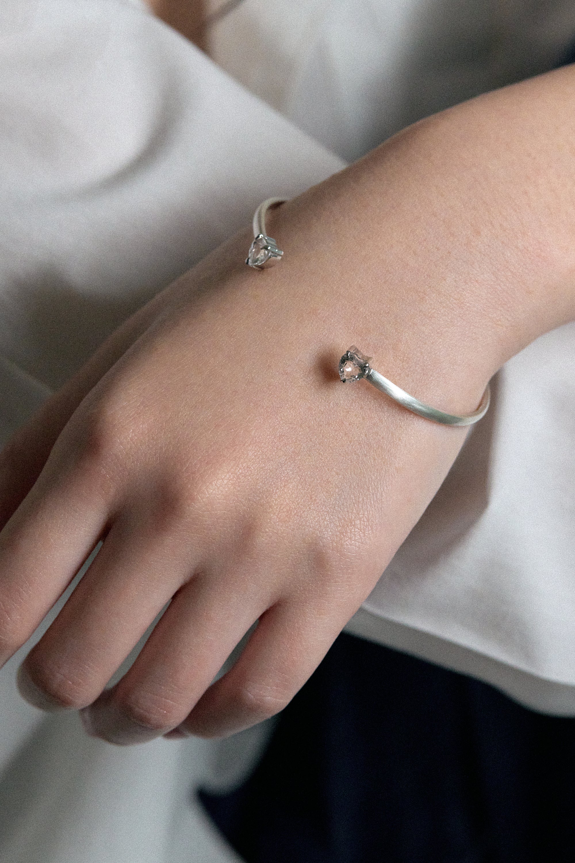 Hand wearing the elegant white noise echo bangle with clear rock crystals on a soft fabric background.