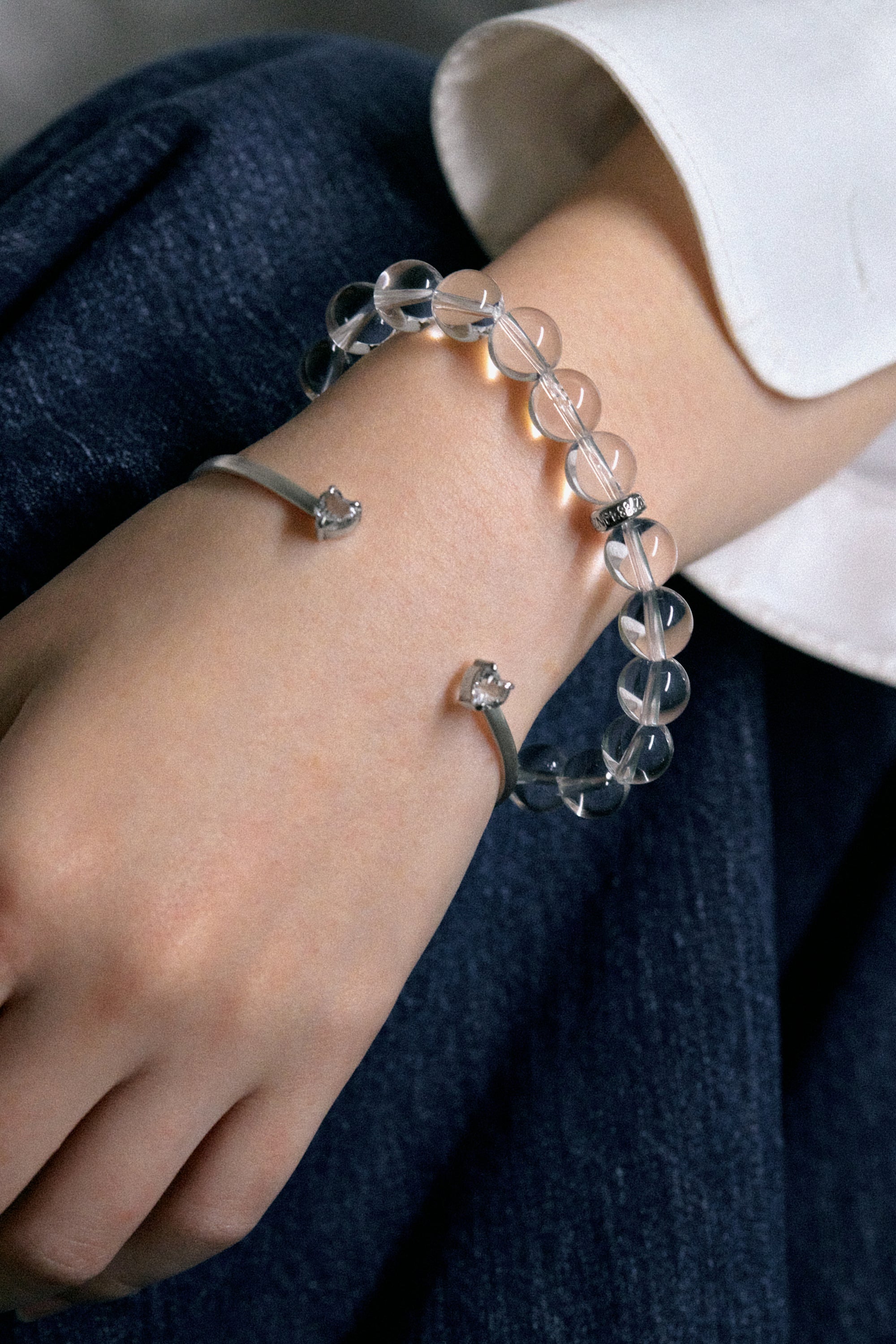 A close-up of a hand wearing the white noise echo bangle and a bead bracelet, showcasing sleek silver and crystal designs.