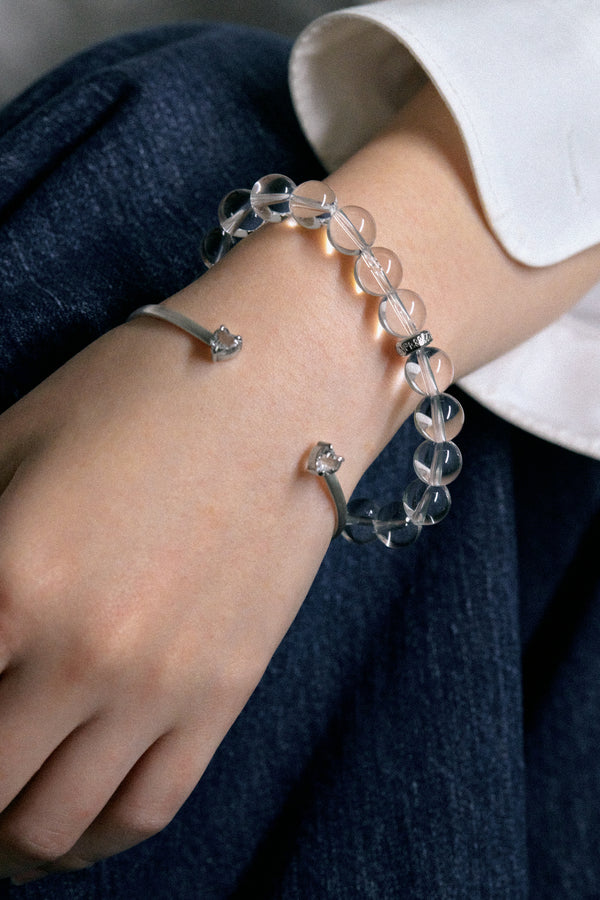 A close-up of a hand wearing the white noise echo bangle and a bead bracelet, showcasing sleek silver and crystal designs.