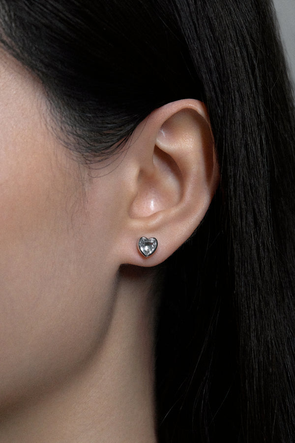 Close-up of a model wearing White Noise Frame Studs, heart-shaped earrings with sparkling crystal detail.