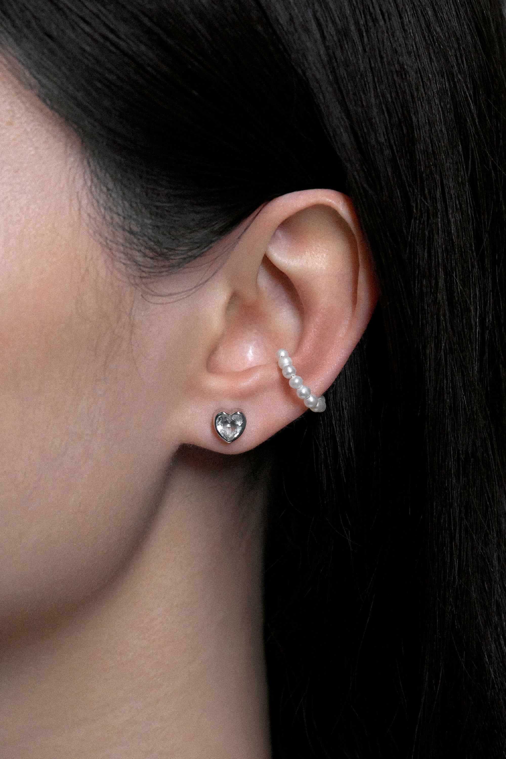 Close-up of a model wearing White Noise Frame Studs in sterling silver with a heart-shaped design and additional pearl earring.