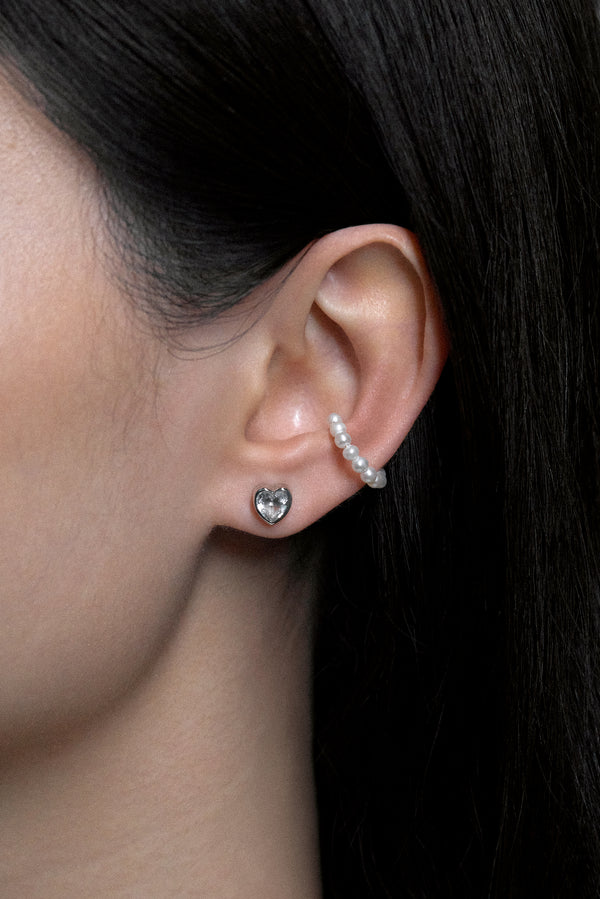 Close-up of a model wearing White Noise Frame Studs in sterling silver with a heart-shaped design and additional pearl earring.
