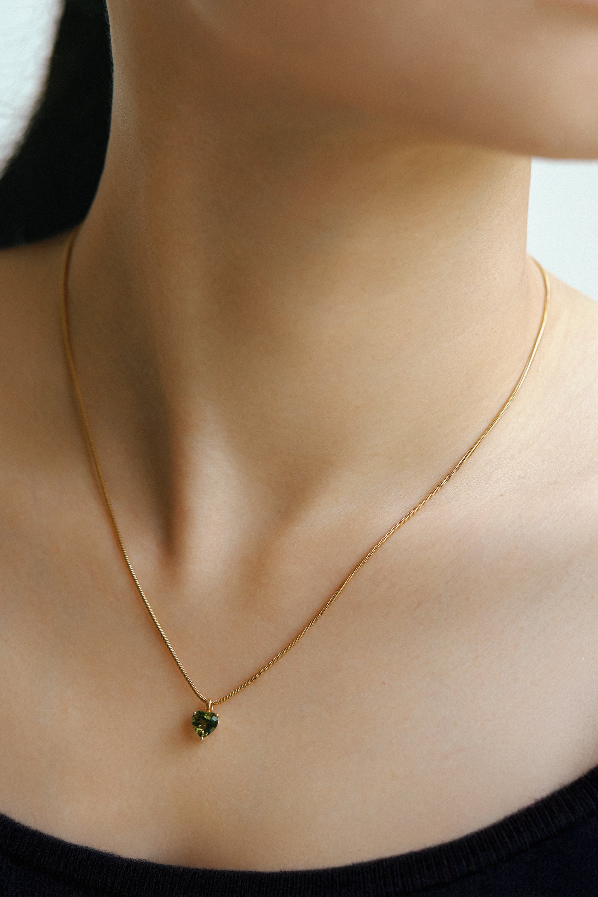 Heart-shaped Moldavite pendant in 18k gold worn on a delicate chain, showcasing its olive-green brilliance.
