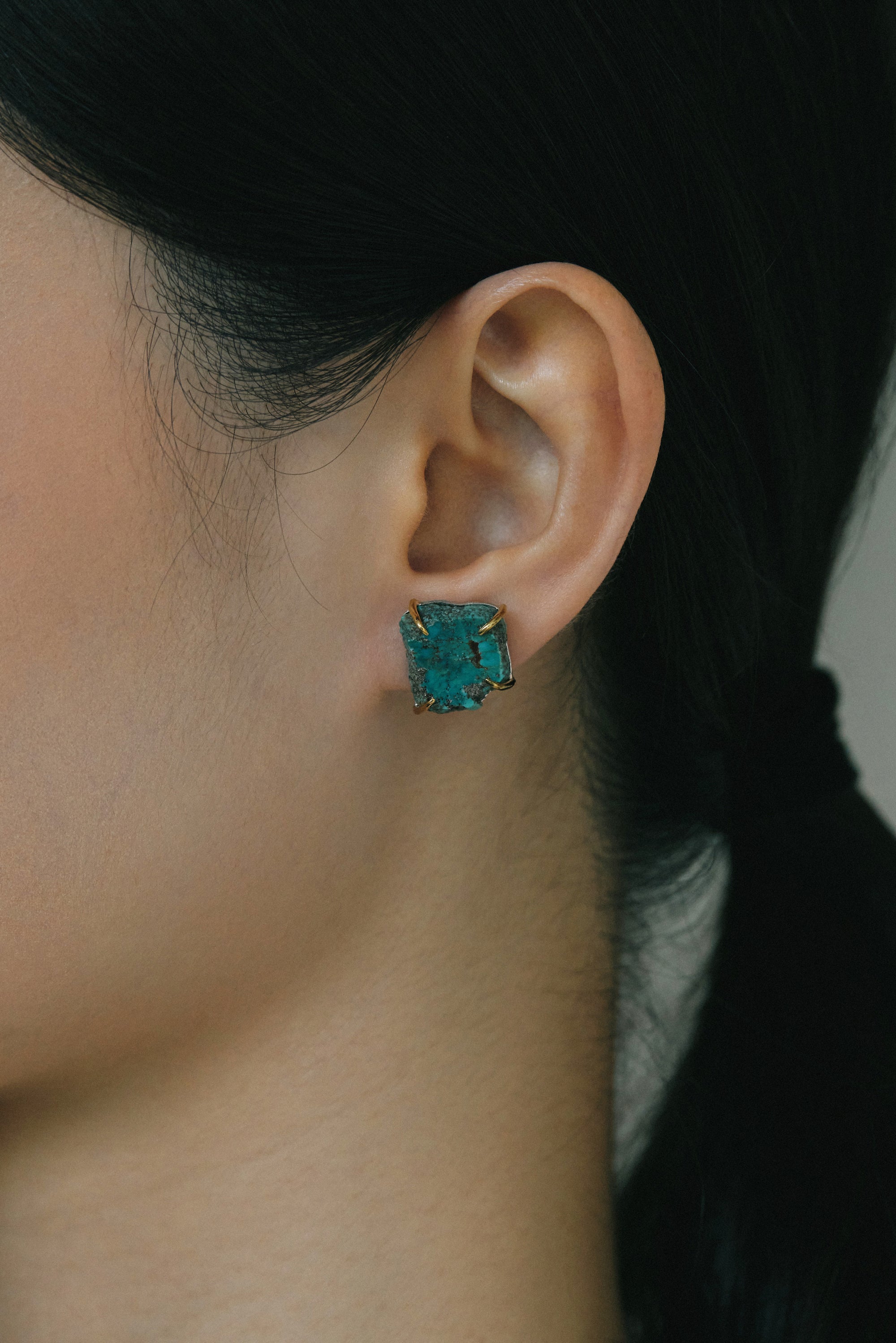 Handmade turquoise ear studs displayed on a model's ear, showcasing organic raw gemstone beauty.