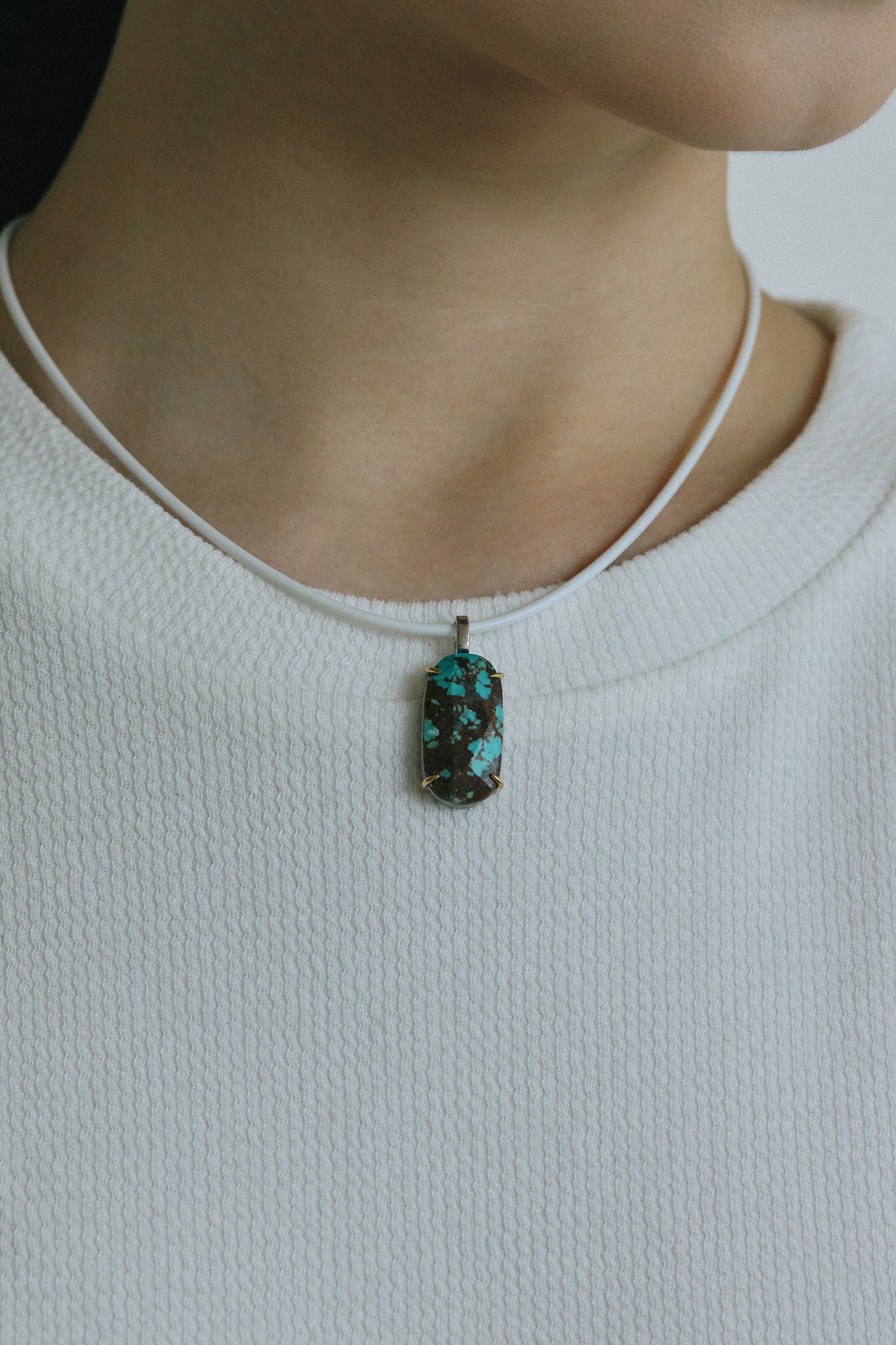 Close-up of a person wearing a raw turquoise pendant on a thin necklace, showcasing its natural beauty.
