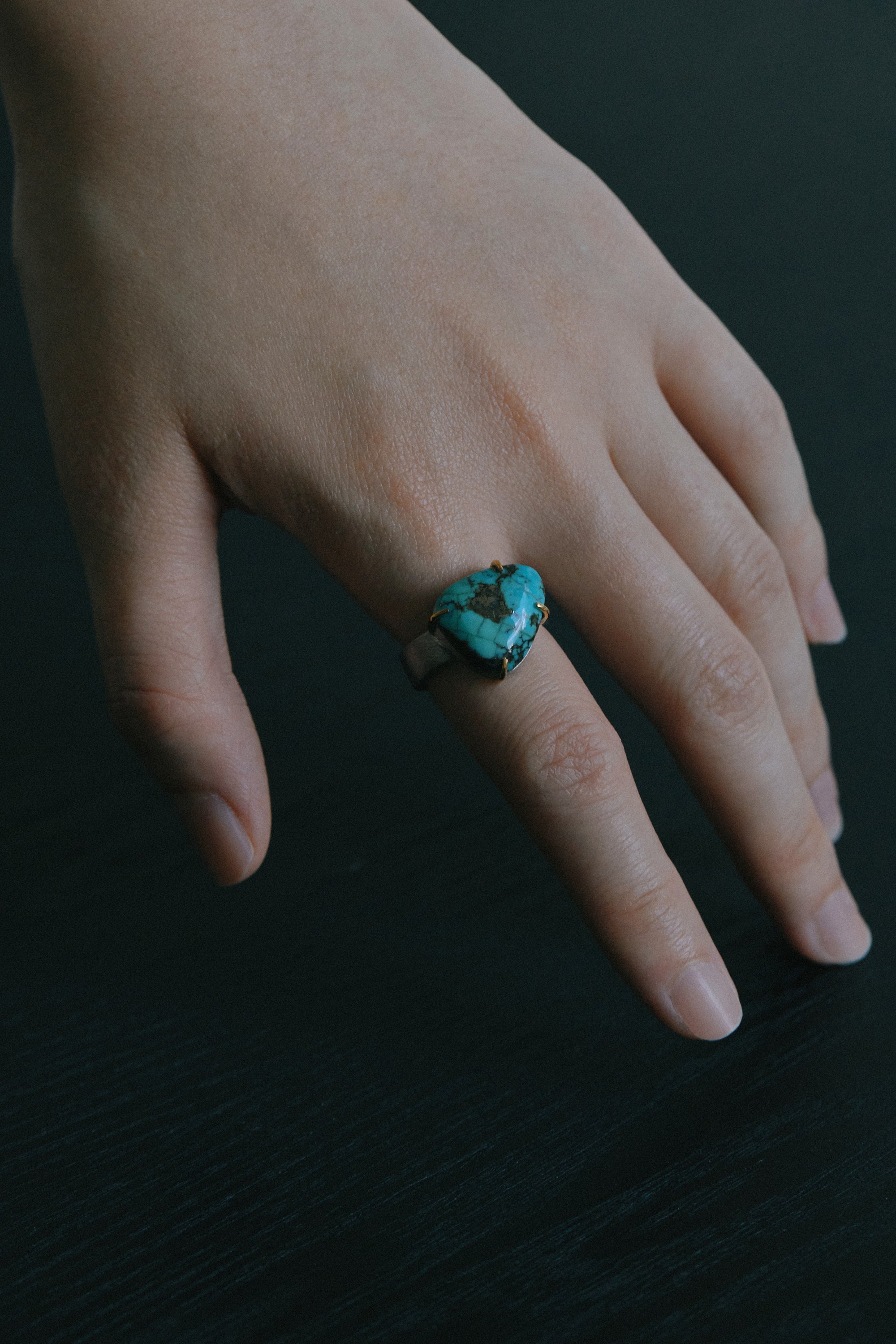 Hand wearing a turquoise handmade open shank ring, showcasing a unique raw turquoise stone against a dark background.